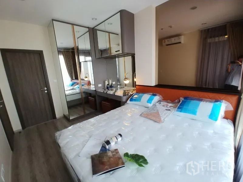 Condominium for rent in Huai Khwang, Bangkok - Bright bedroom with queen bed, mirrored wardrobes, dressing desk, and large window.