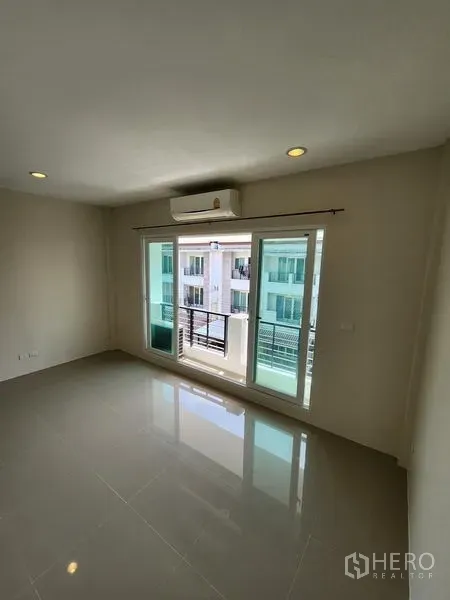 Townhouse for rent in Wang Thonglang, Bangkok - Bright living room with glossy tile floor, sliding glass doors to the balcony and an air conditioner.