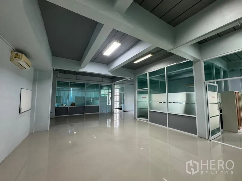 Warehouse for rent or sale in Chon Buri - Large open office space with ceiling lights and several glass offices.