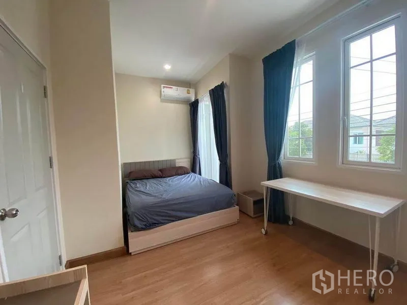 Townhouse for sale in Saphan Sung, Bangkok - Primary bedroom with double bed, windows on two sides, rolling desk and air conditioner.