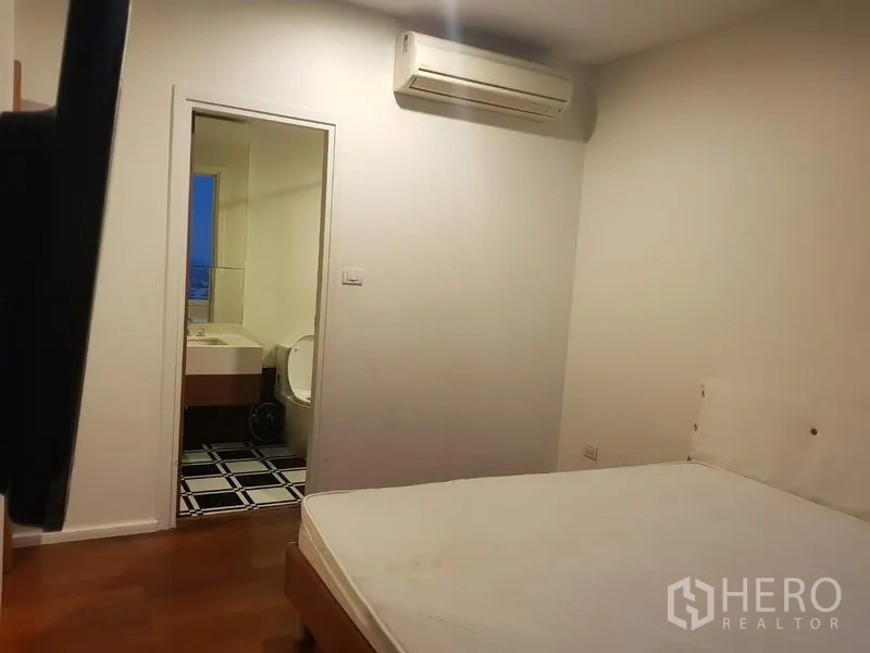 Condominium for rent in Watthana, Bangkok - Secondary bedroom with air conditioner and doorway to an en-suite bathroom, simple neutral decor.