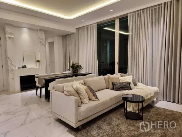 Condominium for sale in Watthana, Bangkok - Open-plan living and dining area with marble floors, recessed lighting, beige sofa and full-height curtains at Royce Private Residences.