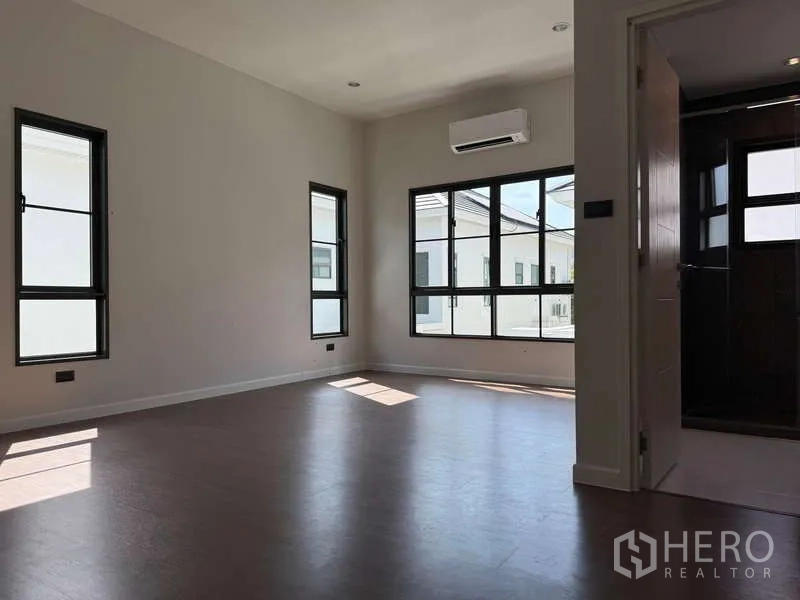 Detached House for rent or sale in Bang Phli, Samut Prakan - Sunlit upstairs bedroom with corner windows and wall-mounted air conditioner.