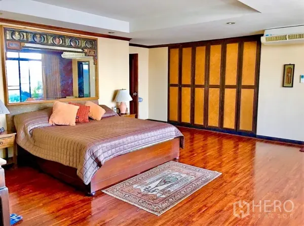 Condominium for rent or sale in Watthana, Bangkok - Spacious master bedroom with hardwood floors, large mirror headboard, and a wall of built-in wardrobes in a Watthana condo.