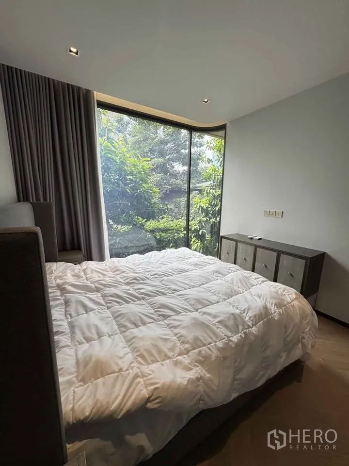 Condominium for rent in Watthana, Bangkok - Bedroom with large bed, console and floor-to-ceiling window facing greenery.