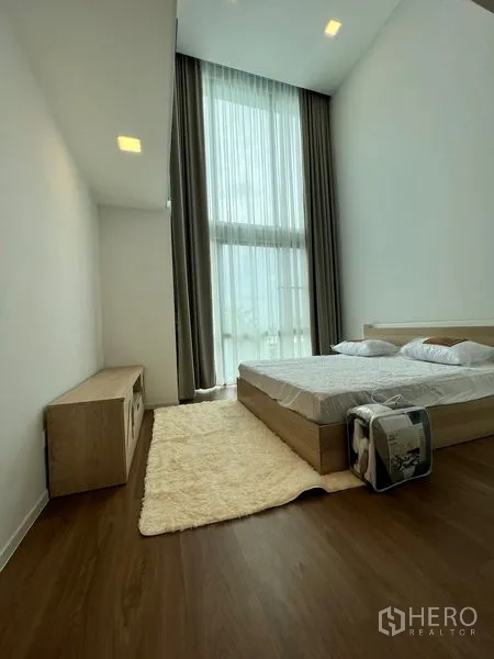 Detached House for rent or sale in Saphan Sung, Bangkok - Minimal bedroom with high ceiling, tall sheer curtains and warm wood flooring.