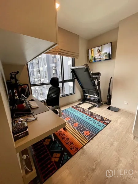 คอนโด ขาย - มุมโฮมออฟฟิศและออกกำลังกาย มีทีวีติดผนัง โต๊ะทำงาน และหน้าต่างกว้าง