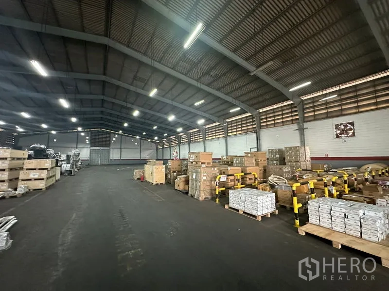 คลังสินค้า ให้เช่าในKhlong Toei, Bangkok - ทางเดินกลางกว้างในโกดังที่มีการระบายอากาศดี พร้อมพาเลทและลังสินค้าภายใต้แสงไฟสว่าง.