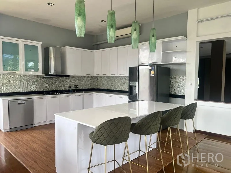 Detached House for sale in Prawet, Bangkok - Modern white kitchen with island, bar stools, and green pendant lights.
