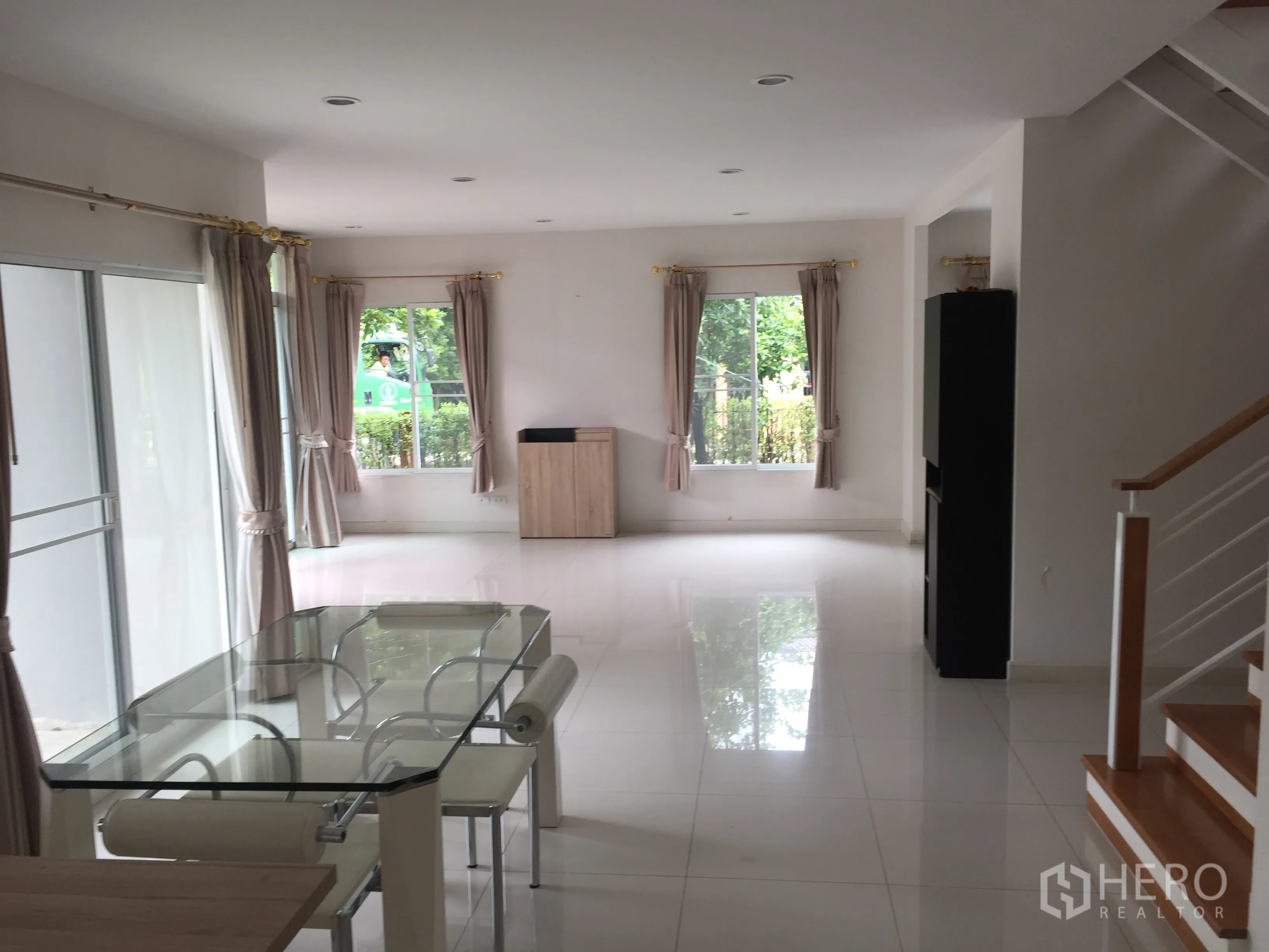 Detached House for rent in Pathum Thani - Open-plan living and dining area with glass dining table, multiple windows and a staircase.