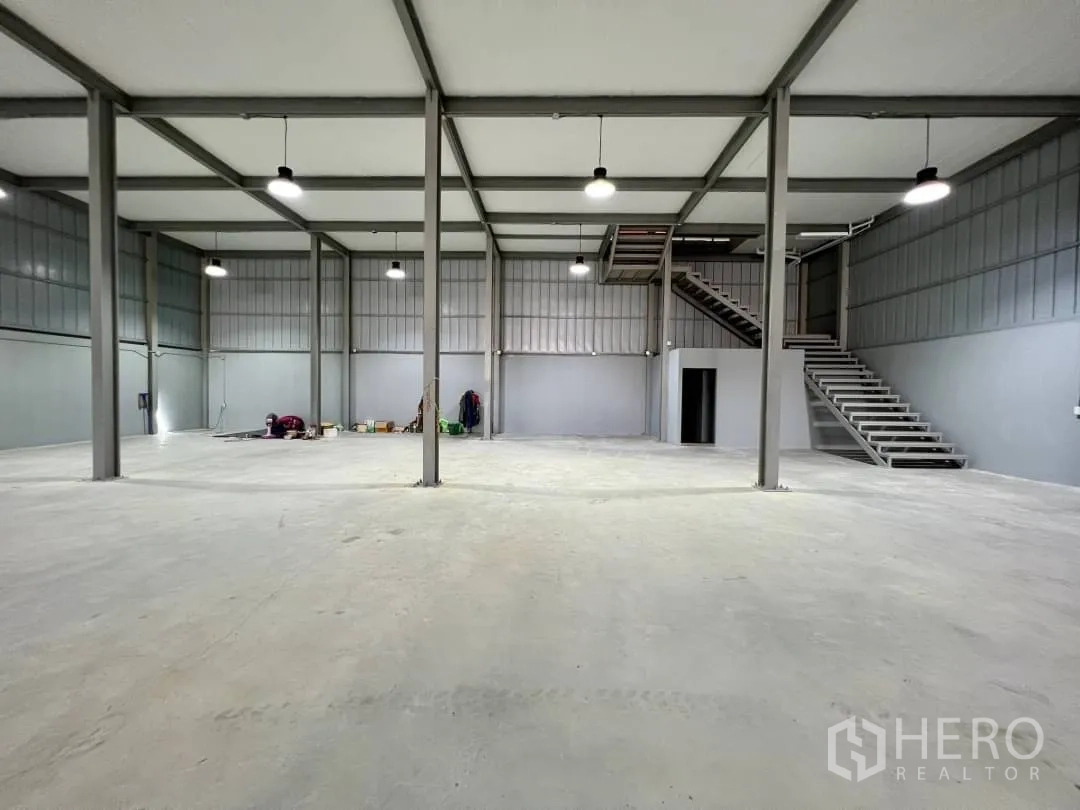 货栈 出租在Sai Mai, Bangkok - 仓库内部空间开阔，钢柱结构，混凝土地面，侧边楼梯通往夹层。