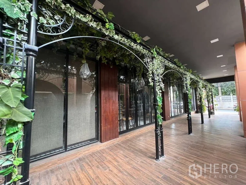 零售空间 出租在Watthana, Bangkok - 玻璃店面前的有顶走廊，铁艺拱架缠绕常春藤。