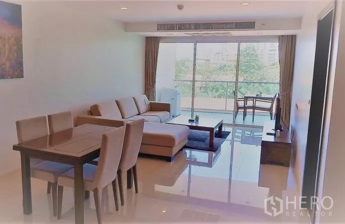 Condominium for sale in Bang Lamung, Chon Buri - Bright living room with L-shaped sofa and floor-to-ceiling doors opening to a balcony with green views.
