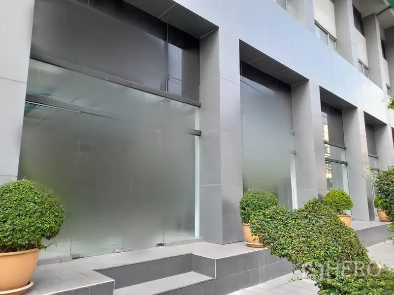 零售空间 出租在Ratchathewi, Bangkok - 拉差贴威现代商铺外立面，大面积磨砂玻璃、灰色立柱与绿植花盆。
