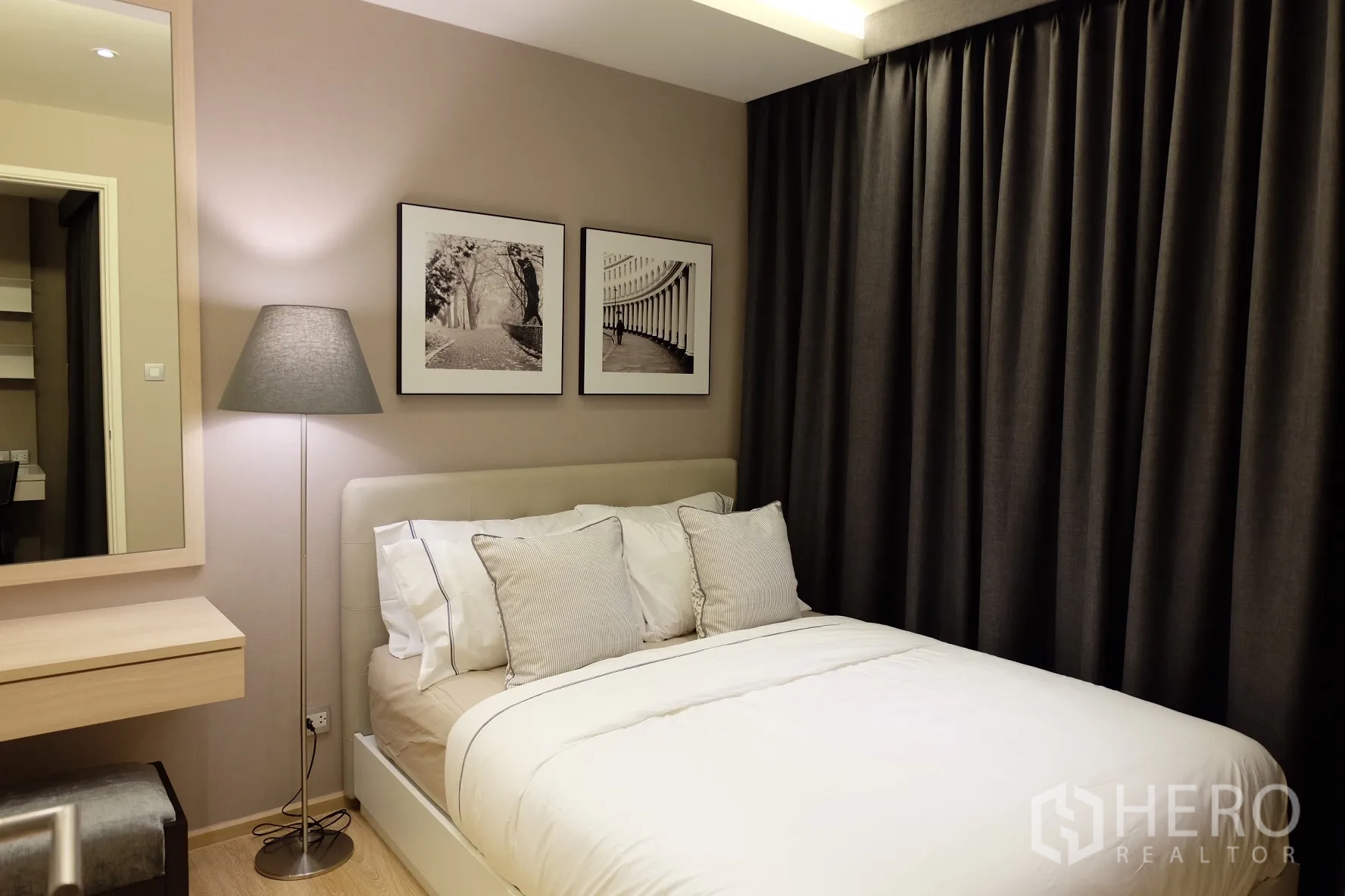 Condominium for rent in Watthana, Bangkok - Stylish bedroom corner featuring framed artwork, dressing table, floor lamp and dark drapes around an upholstered bed.