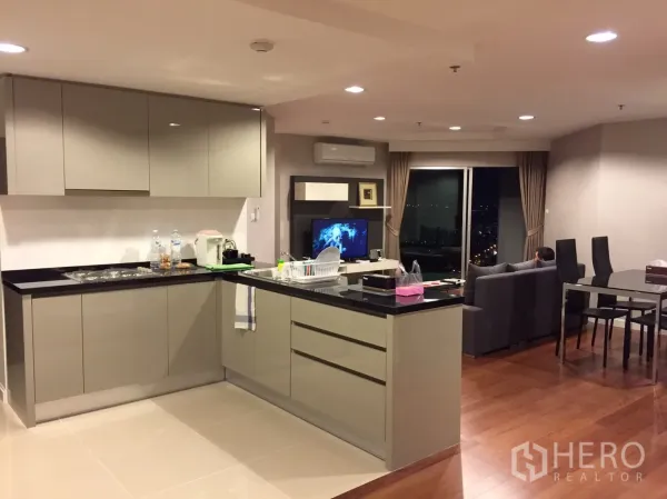 Condominium for rent in Huai Khwang, Bangkok - Modern L-shaped kitchen with glossy cabinets and island beside dining zone.