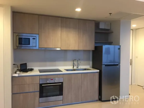 Condominium for rent or sale in Ratchathewi, Bangkok - Modern built-in kitchen with wood cabinetry, oven, cooktop, and stainless refrigerator.