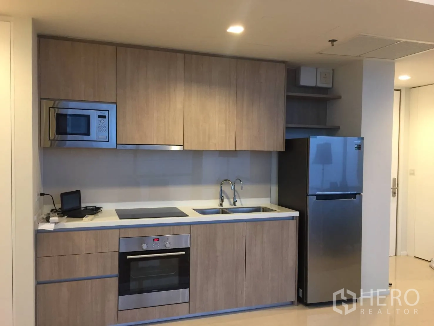 Condominium for rent or sale in Ratchathewi, Bangkok - Modern built-in kitchen with wood cabinetry, oven, cooktop, and stainless refrigerator.