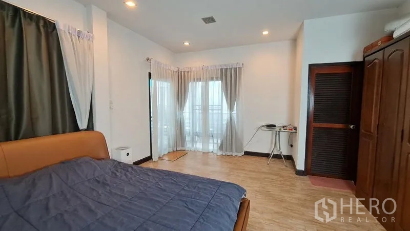 Detached House for rent in Saphan Sung, Bangkok - Master bedroom from another angle showing closet door and bright windows.