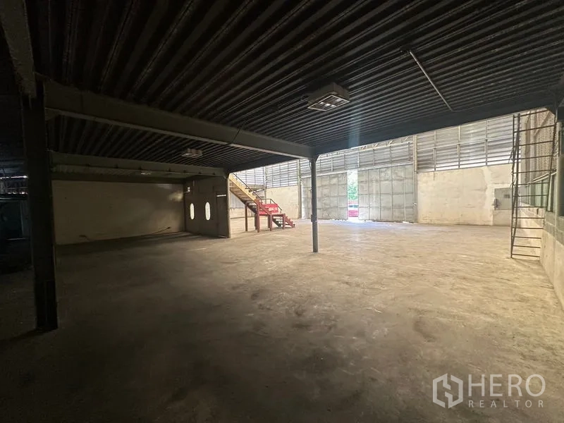 Warehouse for rent in Suan Luang, Bangkok - Covered loading and storage area beneath the mezzanine with large sliding doors and metal columns.