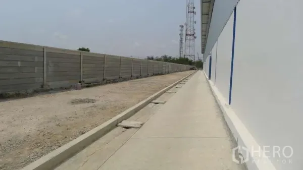 货栈 出租在Bang Phli, Samut Prakan - 仓库外侧人行道与服务车道，旁为混凝土围墙。