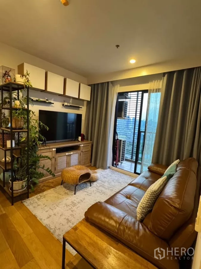 Condominium for rent in Watthana, Bangkok - Cozy living room with leather sofa, TV console, wood flooring and balcony city view.