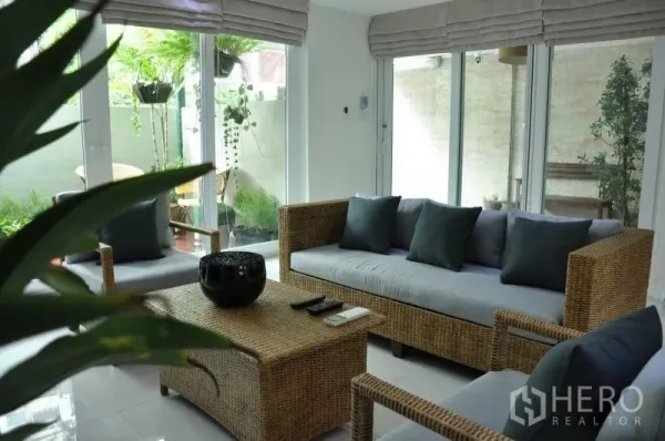 Townhouse for rent or sale in Watthana, Bangkok - Bright sitting room with rattan sofas, floor-to-ceiling glass and a small garden patio.