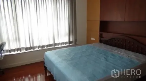 Condominium for rent or sale in Sathon, Bangkok - Bedroom with wooden bed, large curtained window, and hardwood flooring.