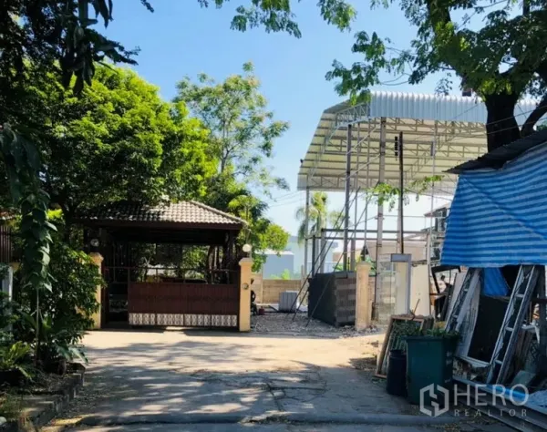Warehouse for rent in Wang Thonglang, Bangkok - Gated driveway with tiled-roof guardhouse and trees beside a new steel-frame warehouse structure in Wang Thonglang.