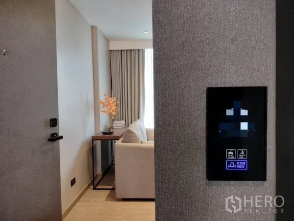 อพาร์ทเมนท์ ให้เช่าหรือขาย - มุมทางเข้าอพาร์ตเมนต์พร้อมแผงควบคุมสัมผัสอัจฉริยะ เห็นโซฟาและแสงธรรมชาติ