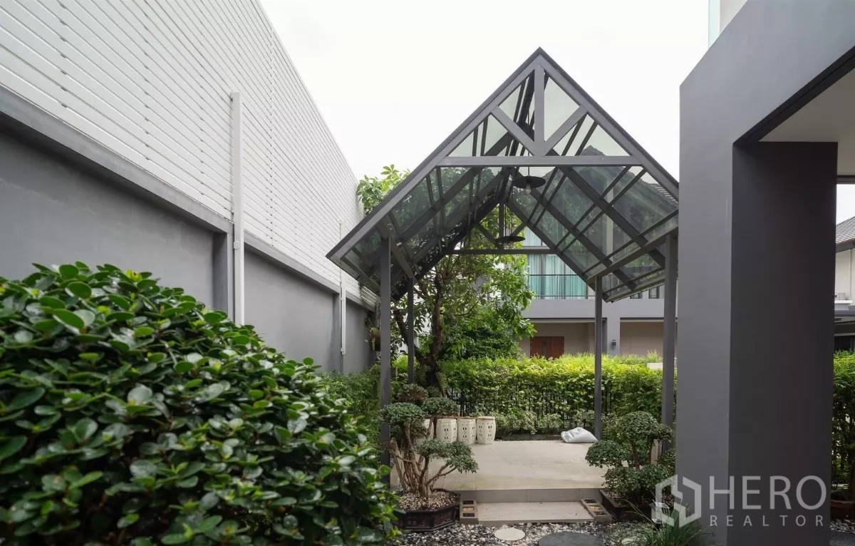 Detached House for rent or sale in Saphan Sung, Bangkok - Shaded garden pavilion with a glass roof beside lush hedges.