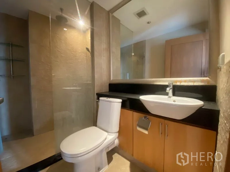 公寓 出租在Sathon, Bangkok - 浴室配玻璃淋浴间、黑色台面的洗手台和坐便器。