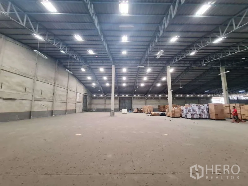 Warehouse for rent - Warehouse space in use with stacked pallets and cartons under bright lights.