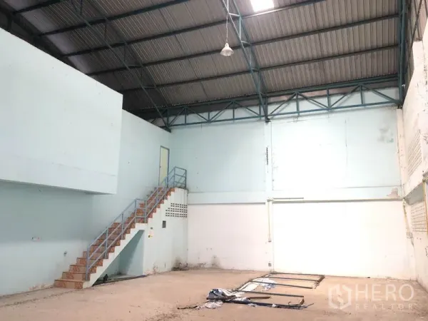 Warehouse for rent in Nonthaburi - Spacious warehouse interior with high steel-truss ceiling and stairs to mezzanine office.