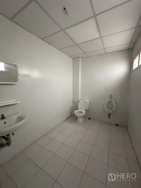 Office Space for rent in Khlong Toei, Bangkok - Clean tiled restroom with toilet, urinal, sink and a small window inside the office.