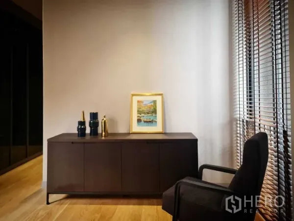 独立式住宅 出售在Lat Phrao, Bangkok - 极简角落，木质边柜、装饰画与扶手椅，旁为百叶窗。