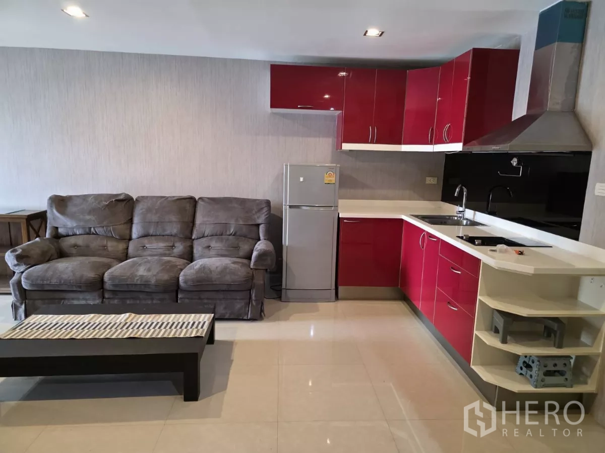 คอนโด ให้เช่าในKhlong Toei, Bangkok - ห้องนั่งเล่นแบบโอเพ่นพร้อมโซฟาสีเทาและครัวรูปตัวแอลสีแดงพร้อมเตาและตู้เย็น