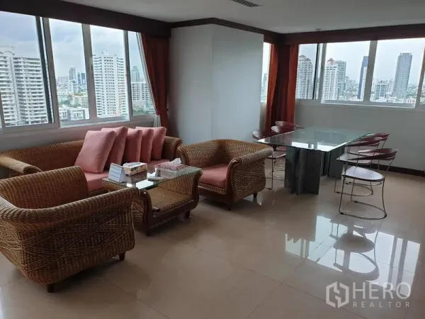 Condominium for rent in Watthana, Bangkok - Bright living and dining area with rattan sofa set, glass dining table, and wide city skyline views through large windows.
