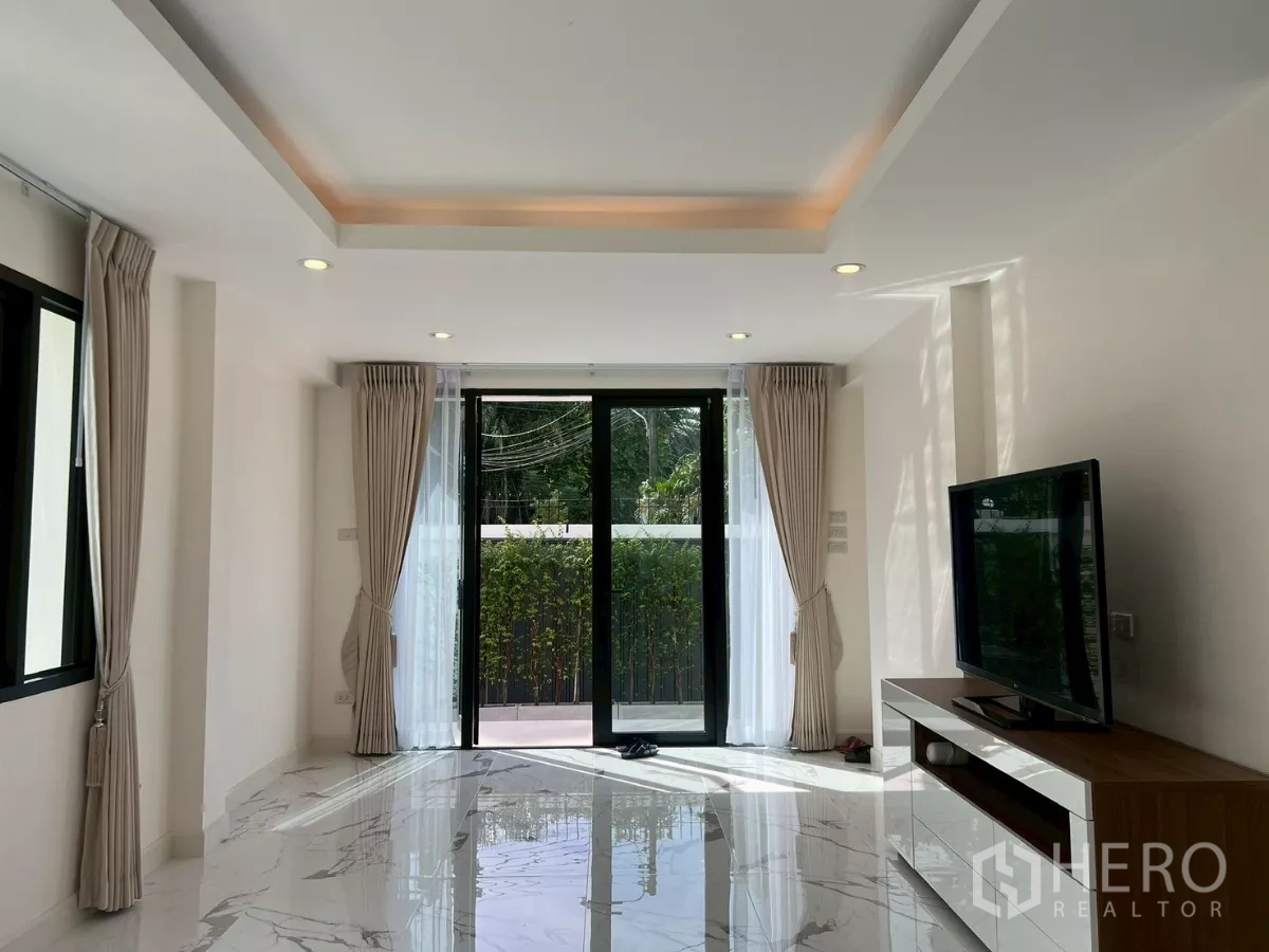 บ้าน ให้เช่าในSuan Luang, Bangkok - ห้องนั่งเล่นมีประตูกระจกบานใหญ่ ตู้วางทีวี และผ้าม่านแบบเต็มความสูง.