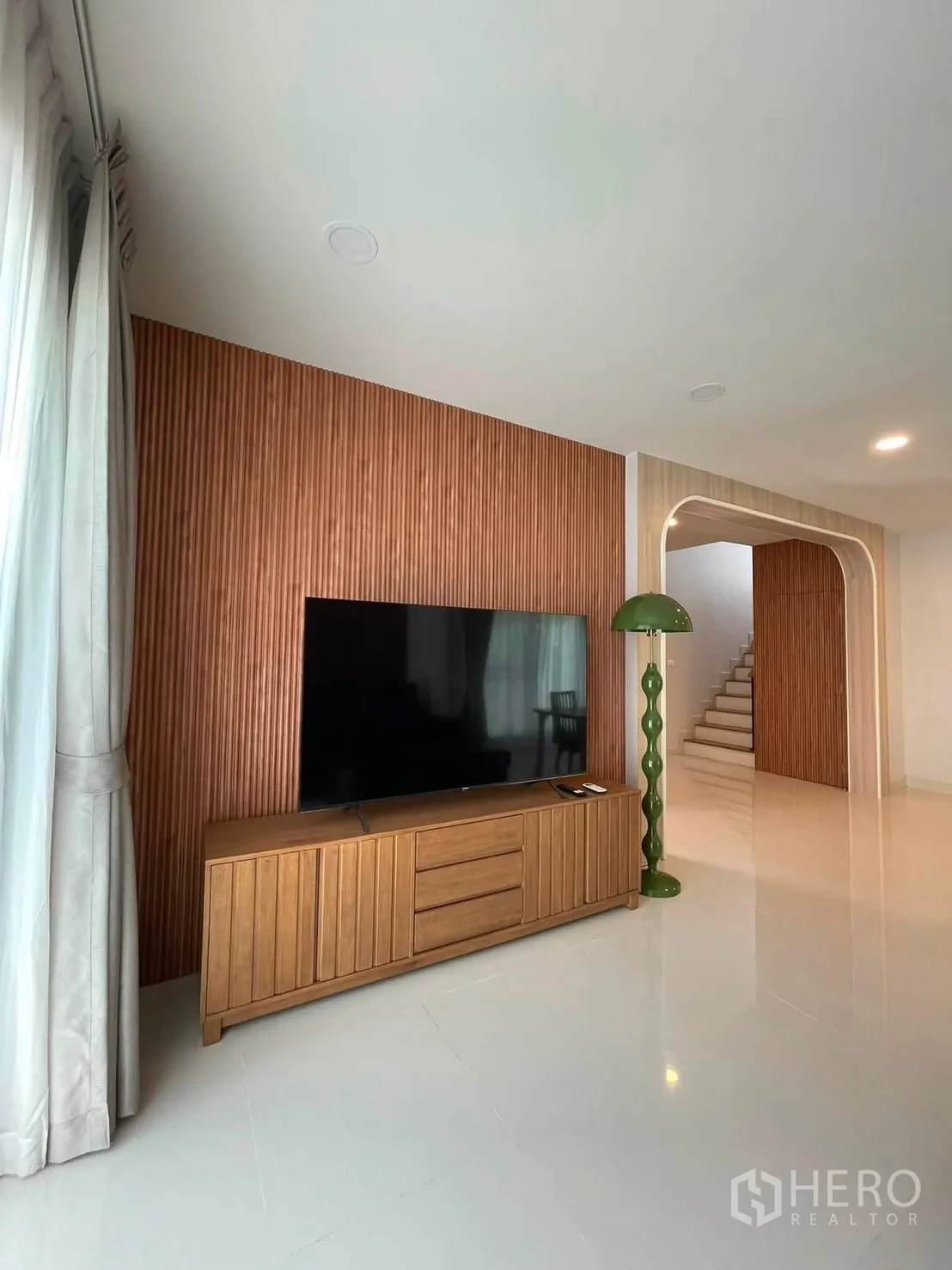 独栋房屋 for rent in Bang Phli, Samut Prakan - 客厅设木质格栅特色墙与电视柜，拱形门洞、亮面地砖和绿色落地灯。