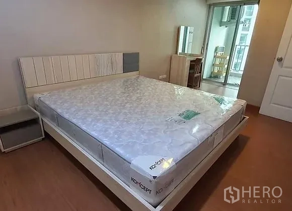 Condominium for rent in Huai Khwang, Bangkok - Master bedroom with large bed, bedside table and access to the balcony.