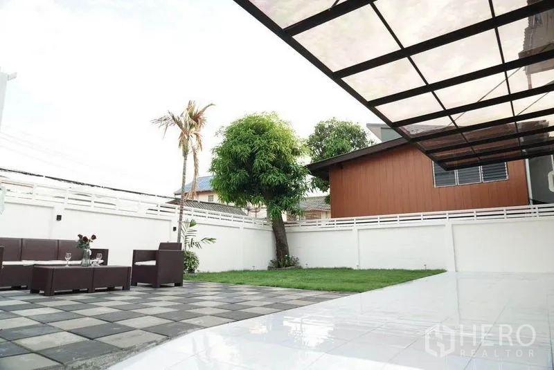 Detached House for sale in Bang Bon, Bangkok - Backyard with shaded patio, green lawn and mature tree enclosed by a privacy wall.