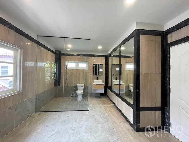 Detached House for sale in Bang Na, Bangkok - Modern bathroom with frameless glass shower, long mirrors and beige tiling.