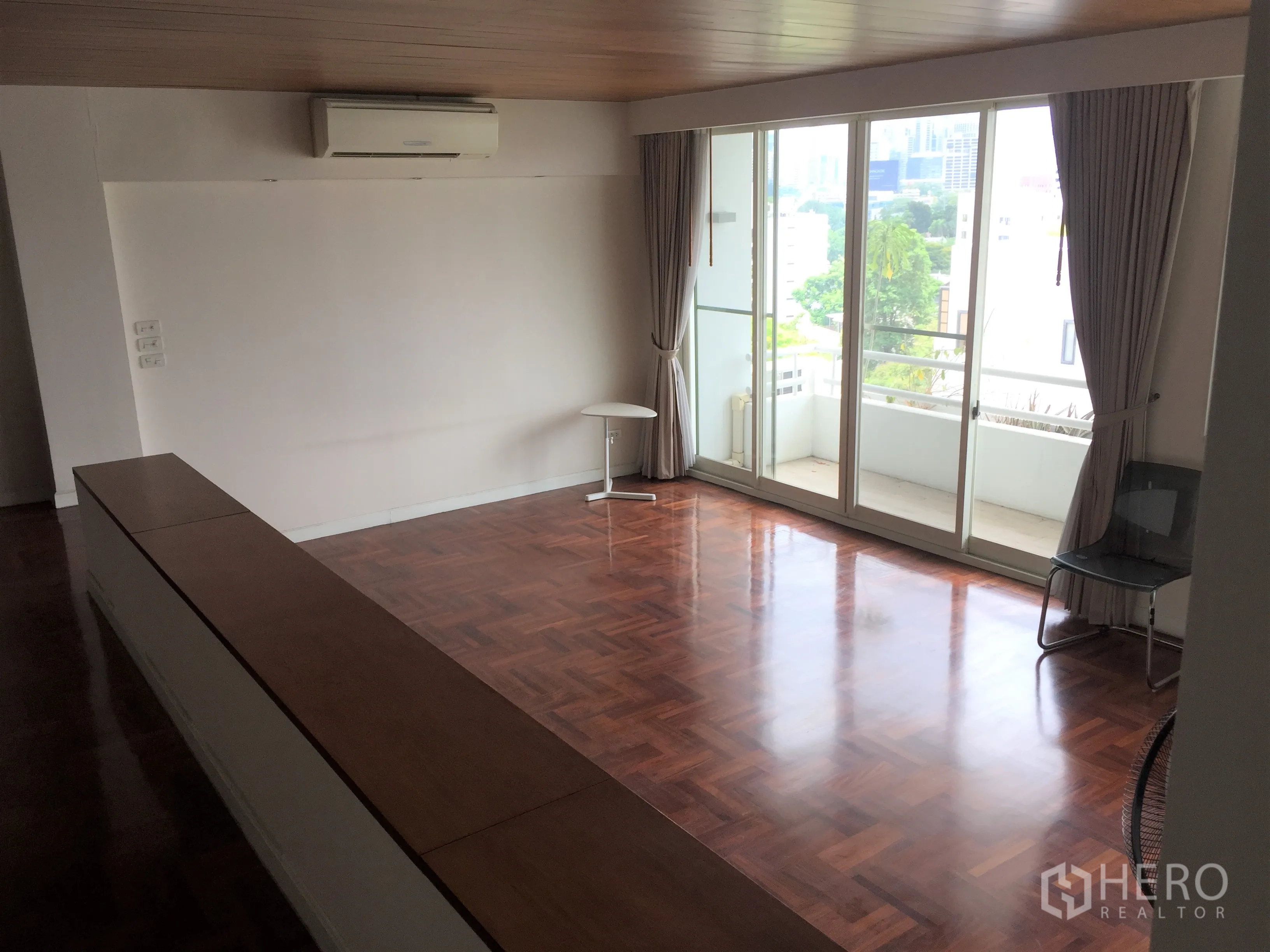 Condominium for rent in Sathon, Bangkok - Large living room with sliding glass doors to a balcony offering green city views and abundant light.
