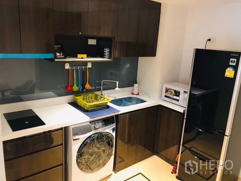 Condominium for rent or sale in Watthana, Bangkok - Fitted kitchen with glossy cabinets, sink, cooktop, microwave, washer and large refrigerator.