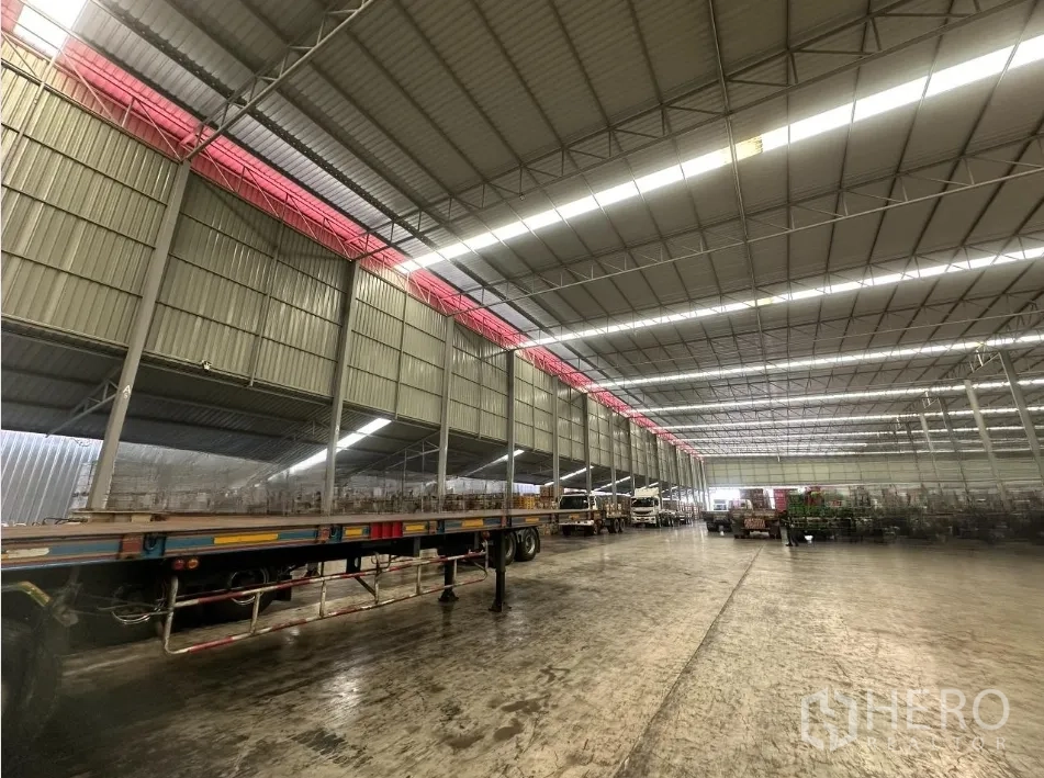 工厂 出租 - 大型厂房仓库内部，钢结构高屋顶与采光带，抛光混凝土地面停有拖挂车。