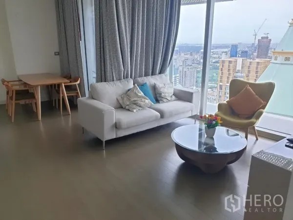 คอนโด ให้เช่าในPathum Wan, Bangkok - โซนพักผ่อนมีโซฟา โต๊ะกลางทรงกลม ชุดทานอาหาร และหน้าต่างสูงจรดเพดานมุมมองเมืองพาโนรามา