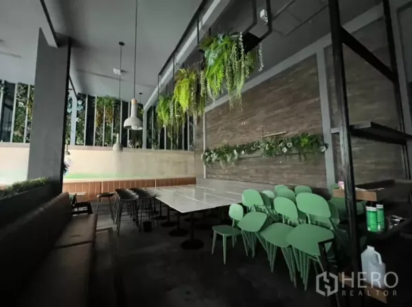 零售空间 出租 - 角落用餐区，石面餐桌、绿色椅子与墙面绿植。