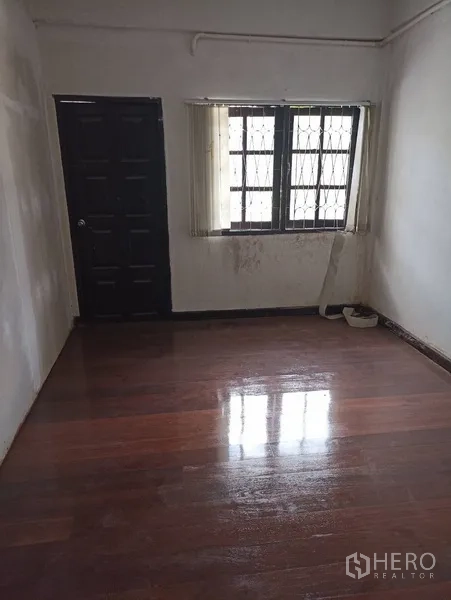 联排别墅 出租或出售在Wang Thonglang, Bangkok - 空房间，抛光木地板，侧门与带防护栏的窗户。