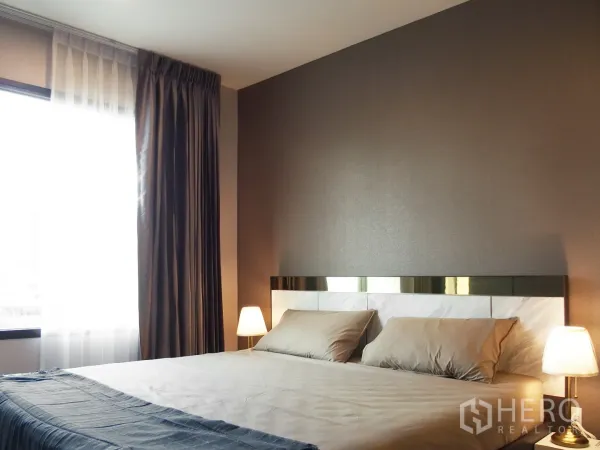 Condominium for rent in Huai Khwang, Bangkok - Bright bedroom with double bed, bedside lamps, and large window with drapes in a Huai Khwang condo.